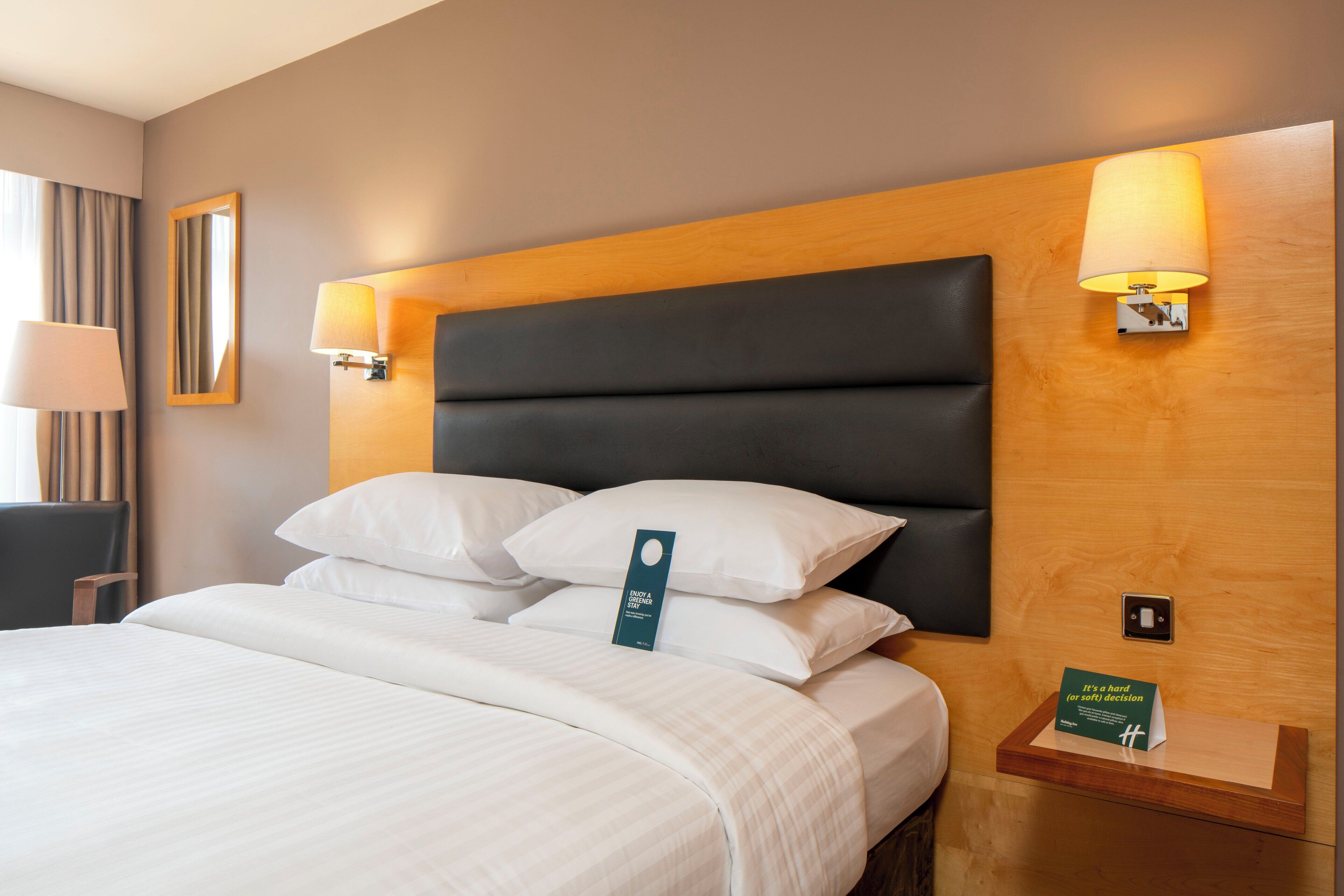 A neatly made bed with white linens, a dark headboard, and two wall-mounted lamps.