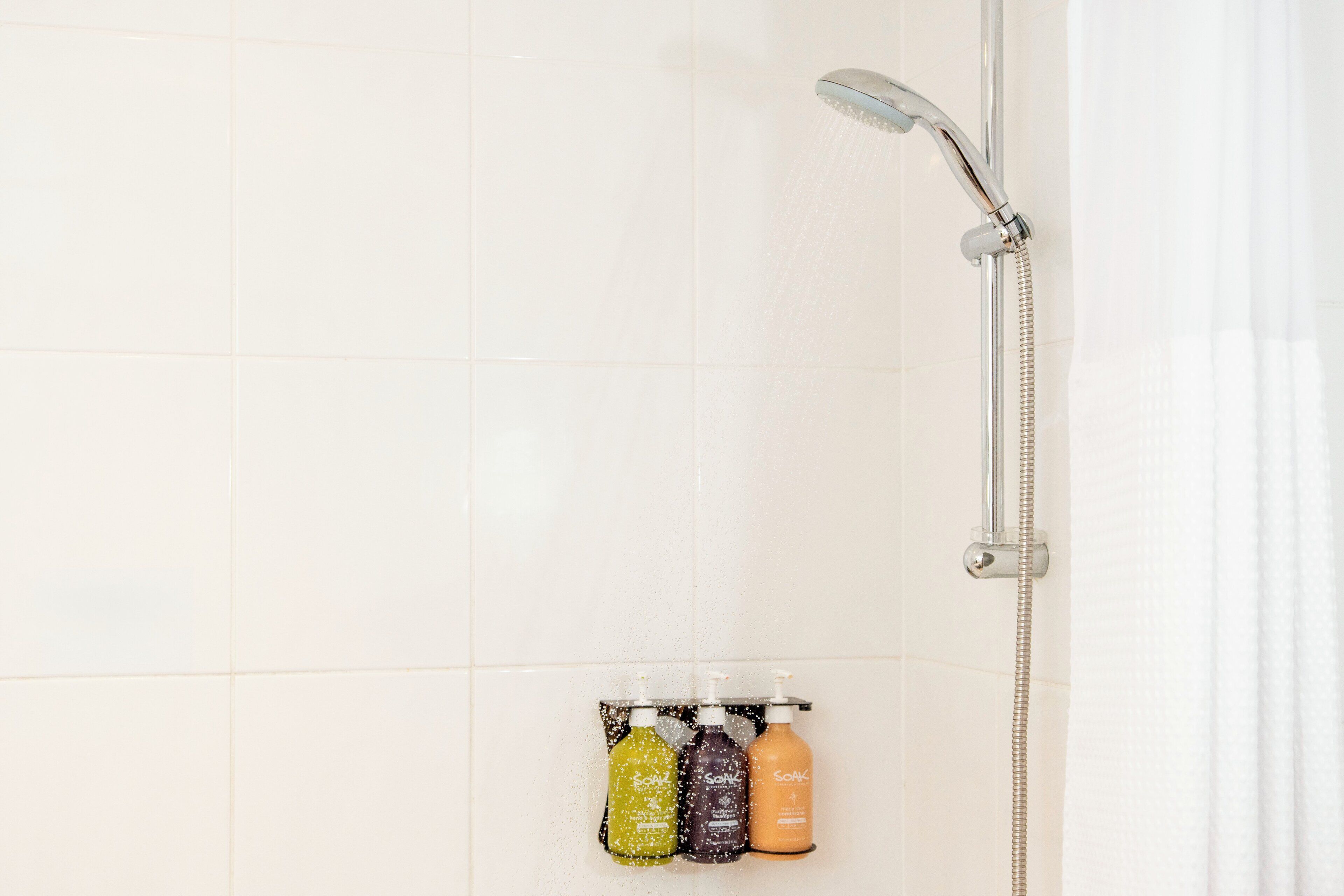 Una ducha con cabezal de ducha manual y dispensador de jabón de pared que contiene tres botellas.