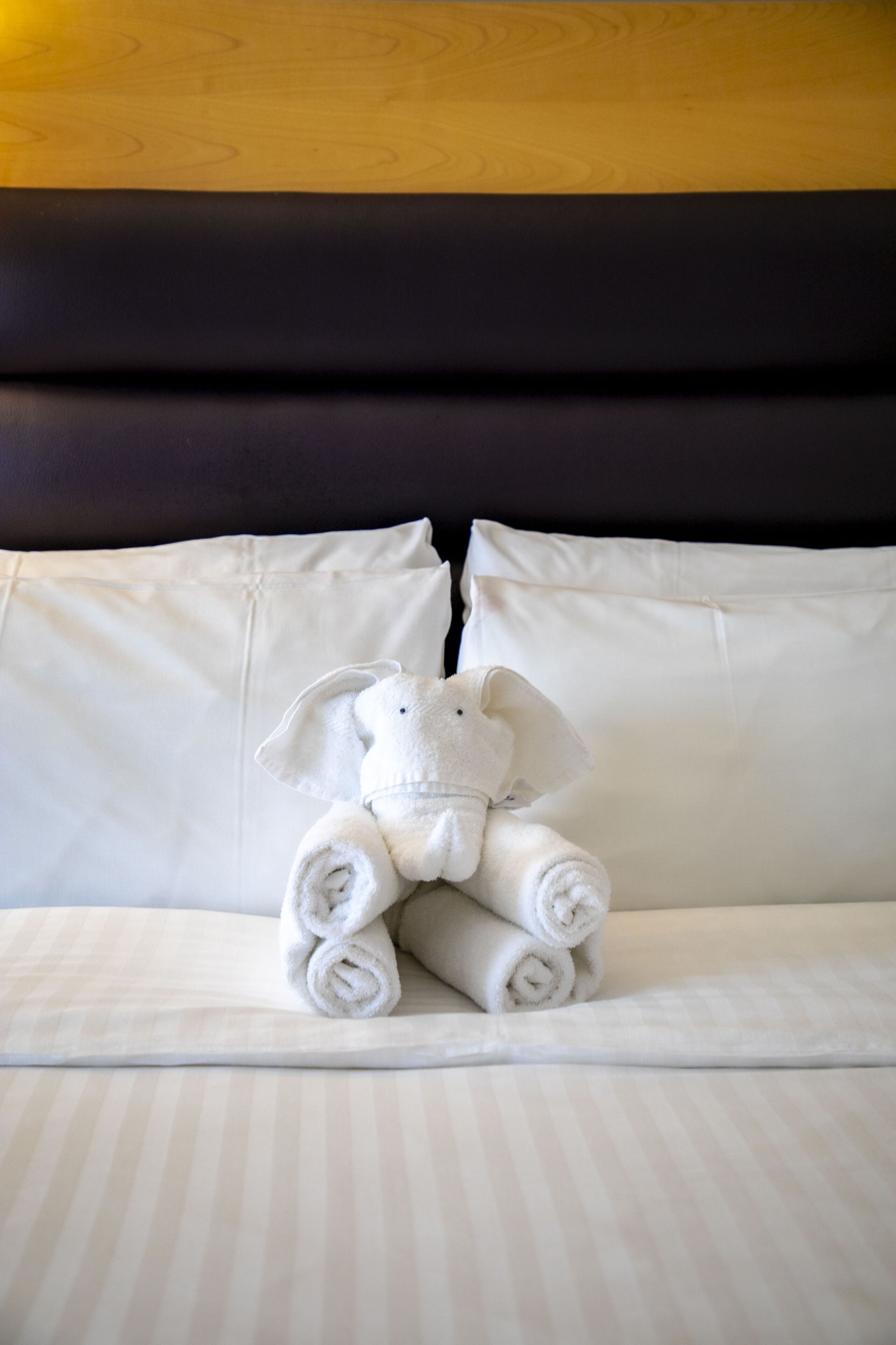 A bed with rolled towels and a stuffed elephant toy.