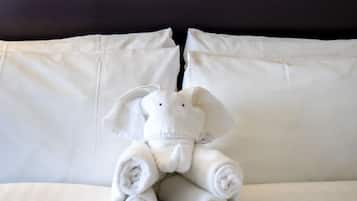 A bed with rolled towels and a stuffed elephant toy.