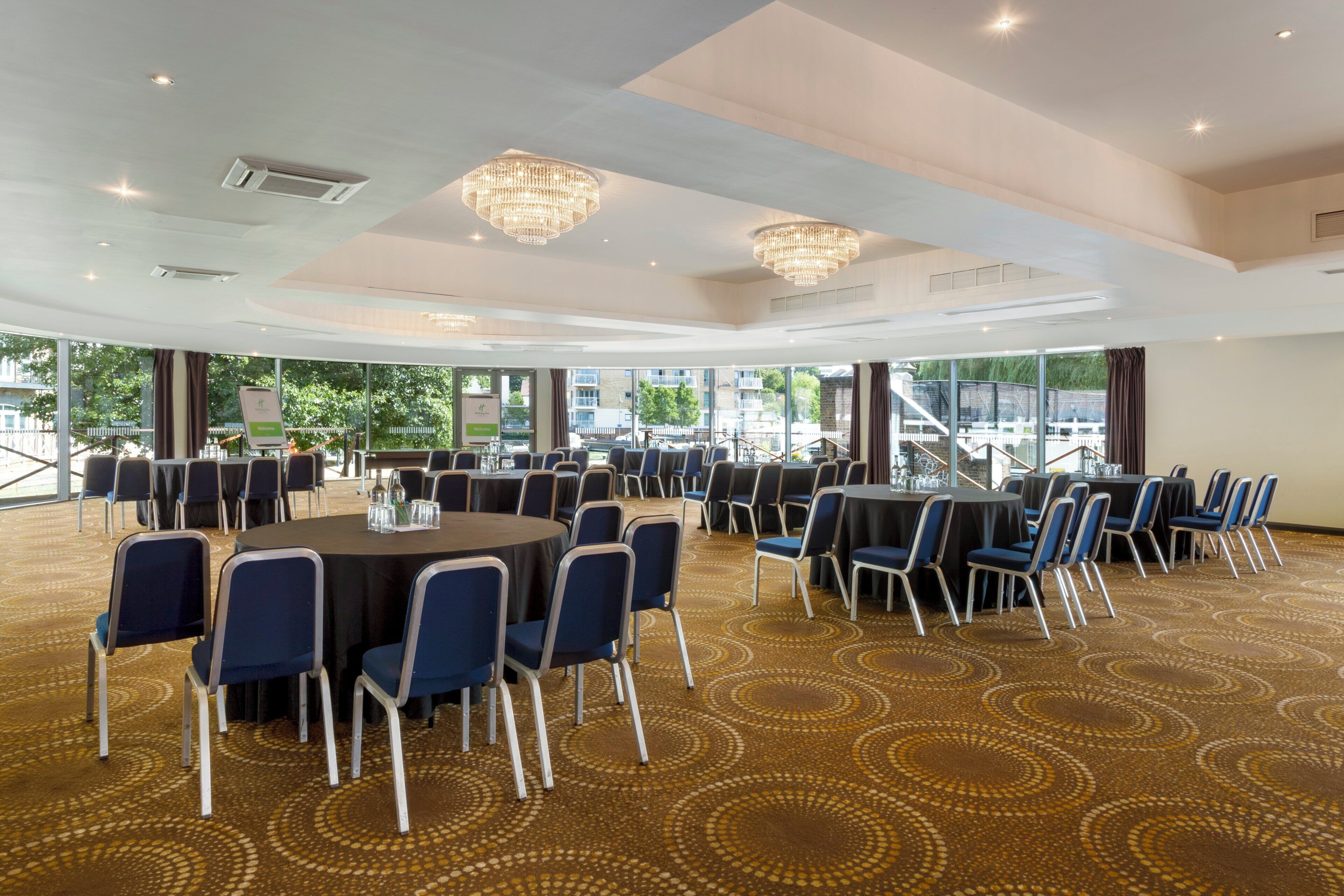A conference room with round tables and chairs, large windows, and a patterned carpet.