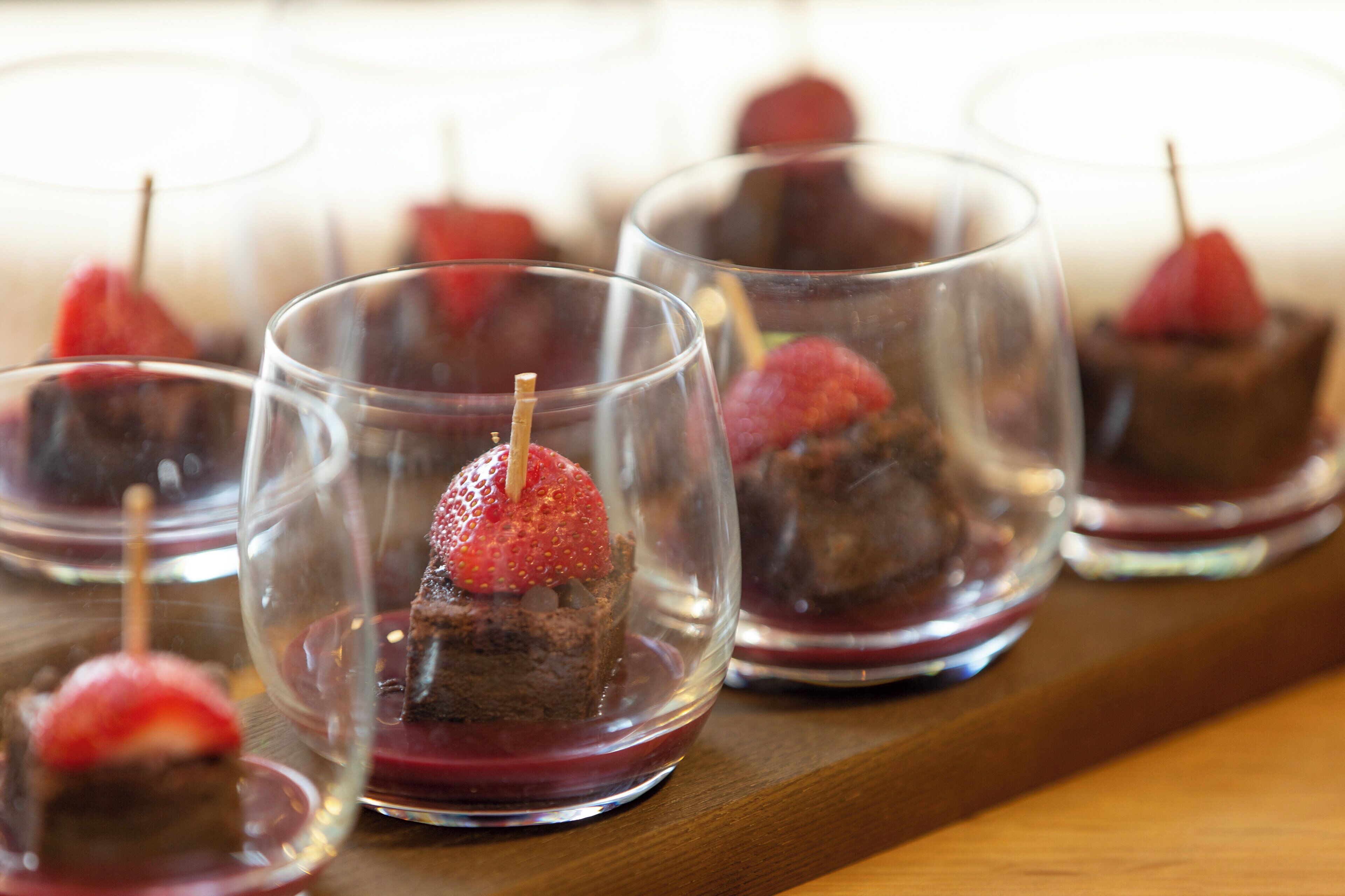 A series of clear glasses containing a dessert with a strawberry on top.
