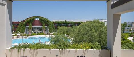 En terrasse med to Adirondack-stole og et bord, med udsigt over en swimmingpool og en bygning med et buet tag.