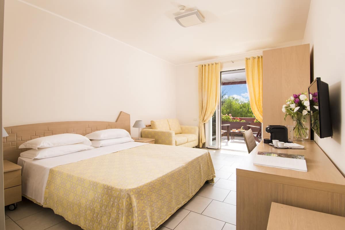 Ein Hotelzimmer mit einem großen Bett, einem Schreibtisch, einem Sessel, einer Couch und Blick ins Freie.