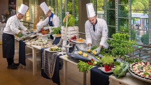 A buffet setup with chefs preparing food, surrounded by large windows offering a view of greenery. - Ethra Reserve - Calanè 4* (Castellaneta)