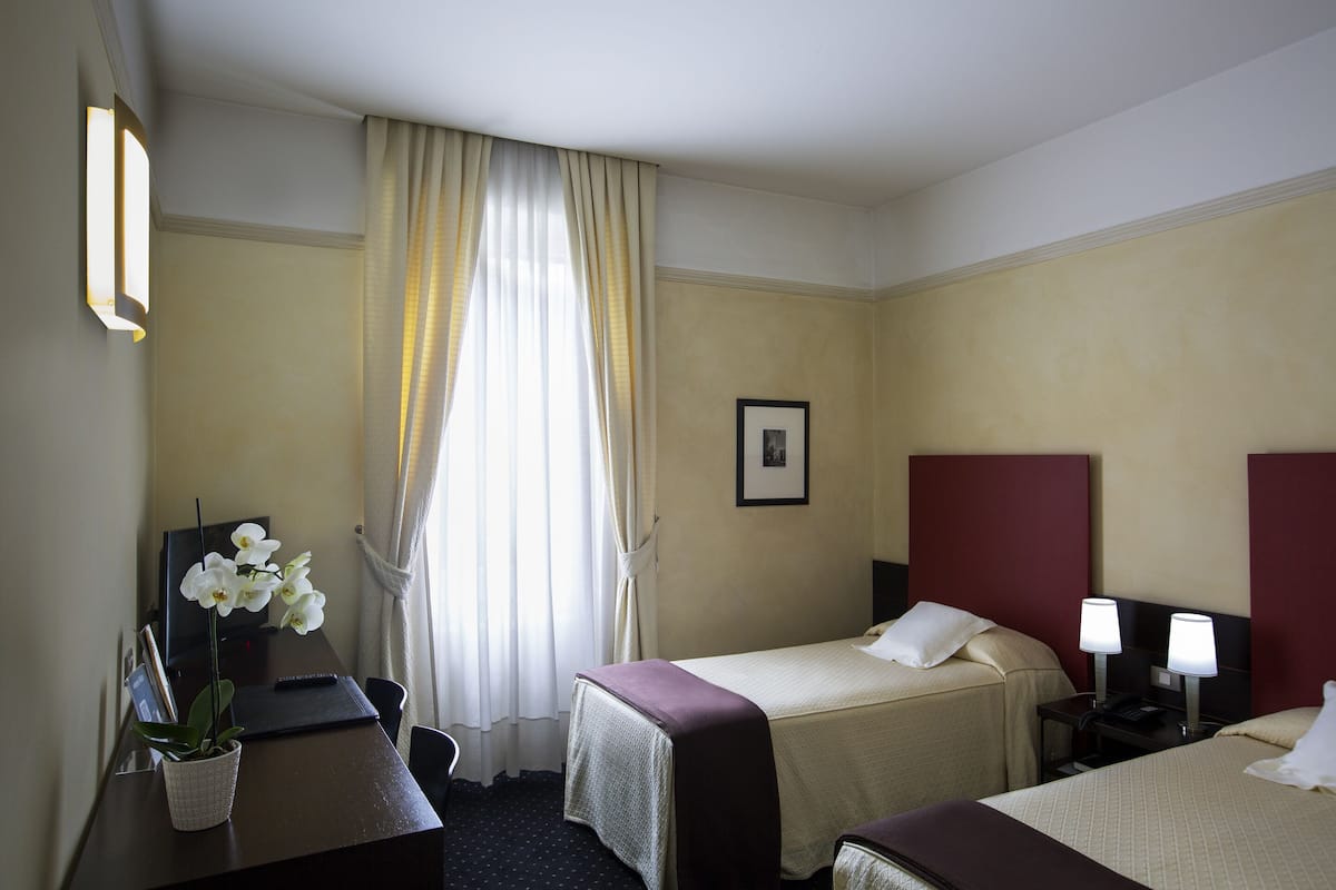A hotel room with two beds, a desk with a computer, a chair, and a window with curtains.