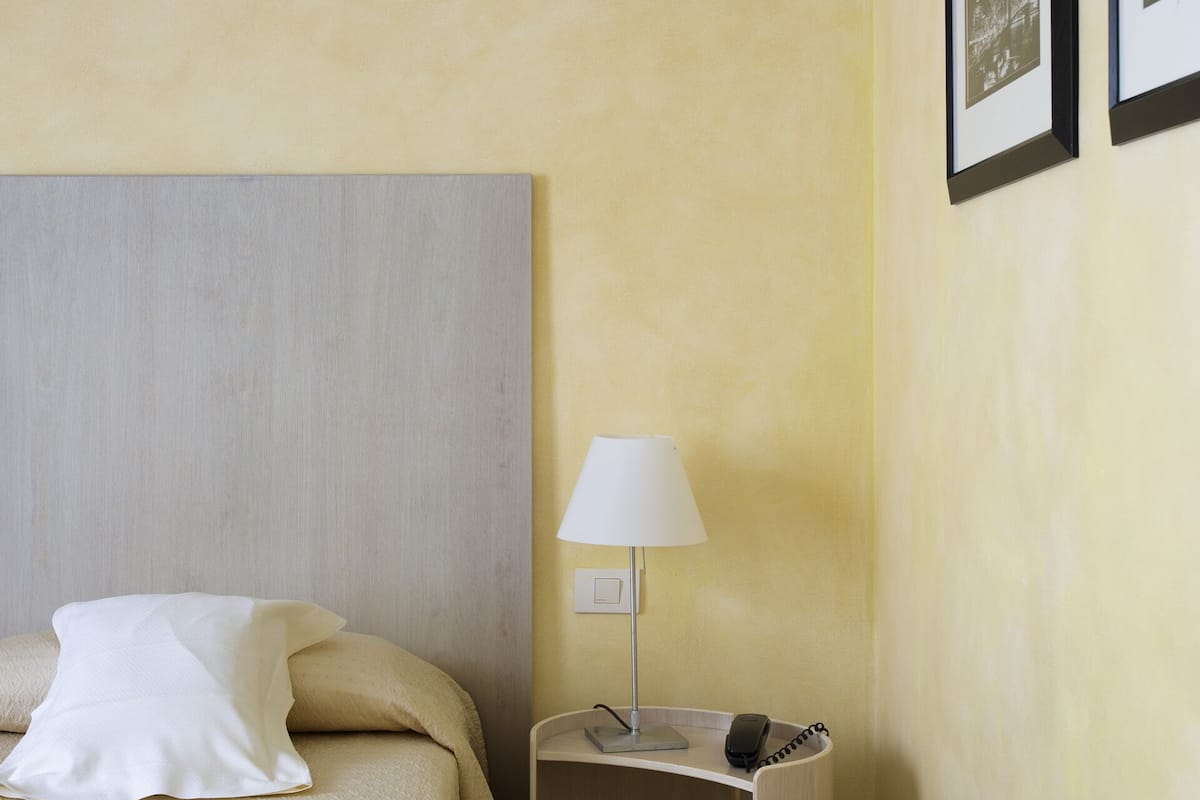 A hotel room with a bed, a bedside table with a lamp, and two framed pictures on the wall.