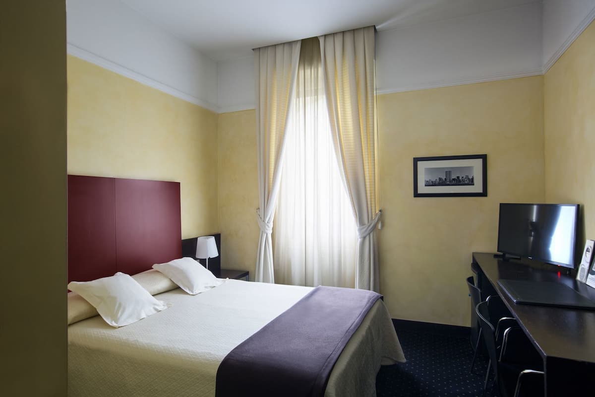 A hotel room with a bed, a desk, a television, and a picture on the wall.