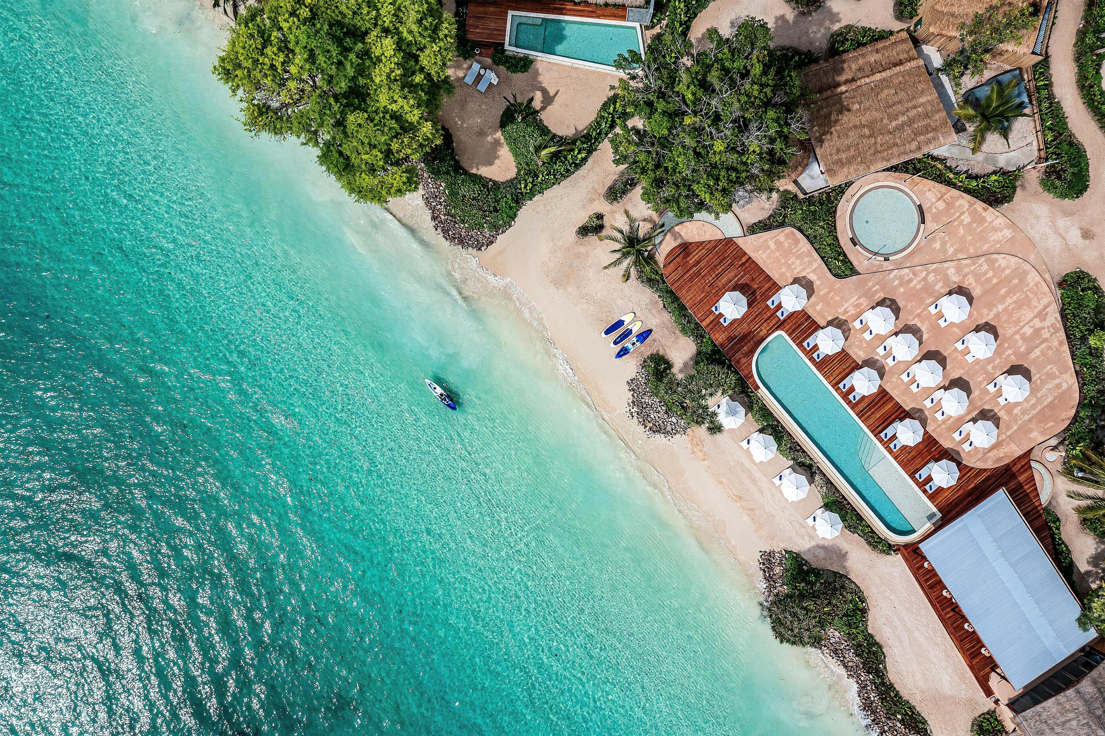 Vista aérea de un resort con una gran piscina, zona de playa y un barco en el agua.