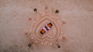 A circular sand art installation with a central table and chairs, surrounded by small lights and greenery.