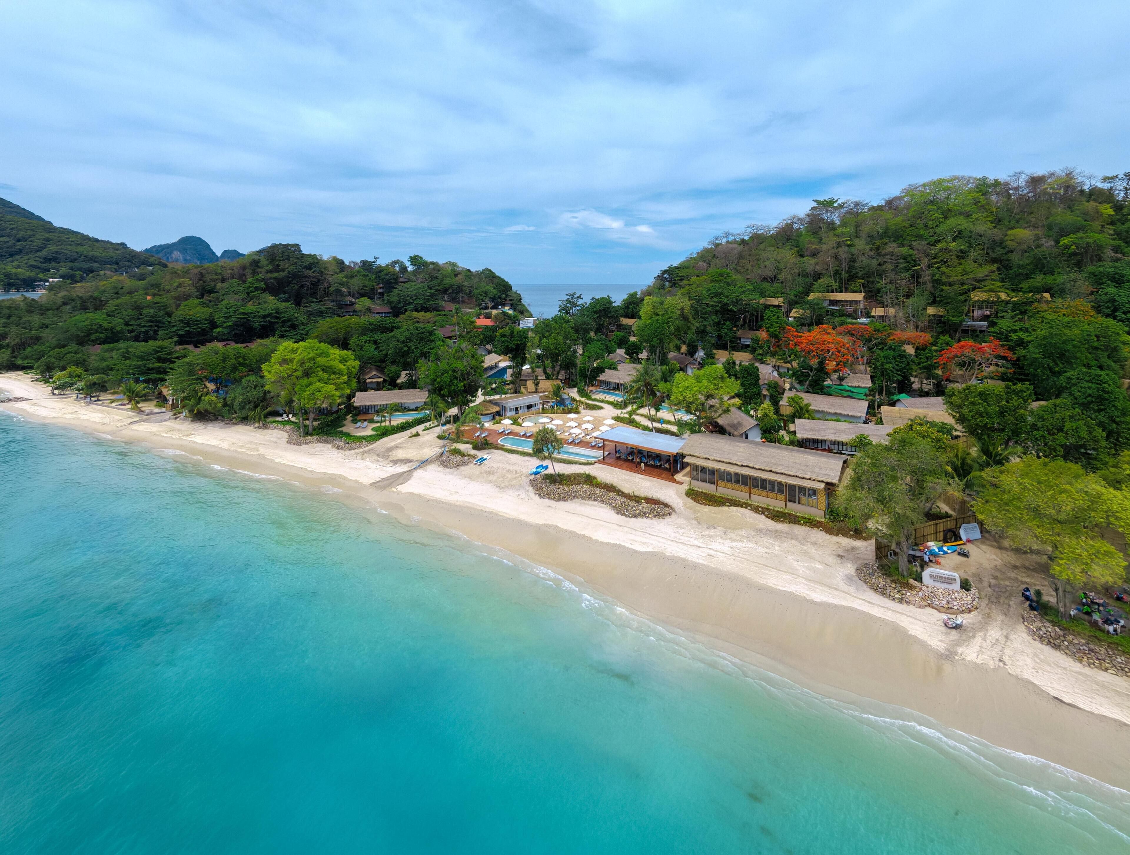 Resort costeiro com acesso à praia, áreas de piscina e diversos edifícios rodeados por vegetação exuberante.