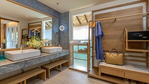 A modern bathroom with a large mirror, dual sinks, wooden benches, a vanity with a basket, and a towel rack.