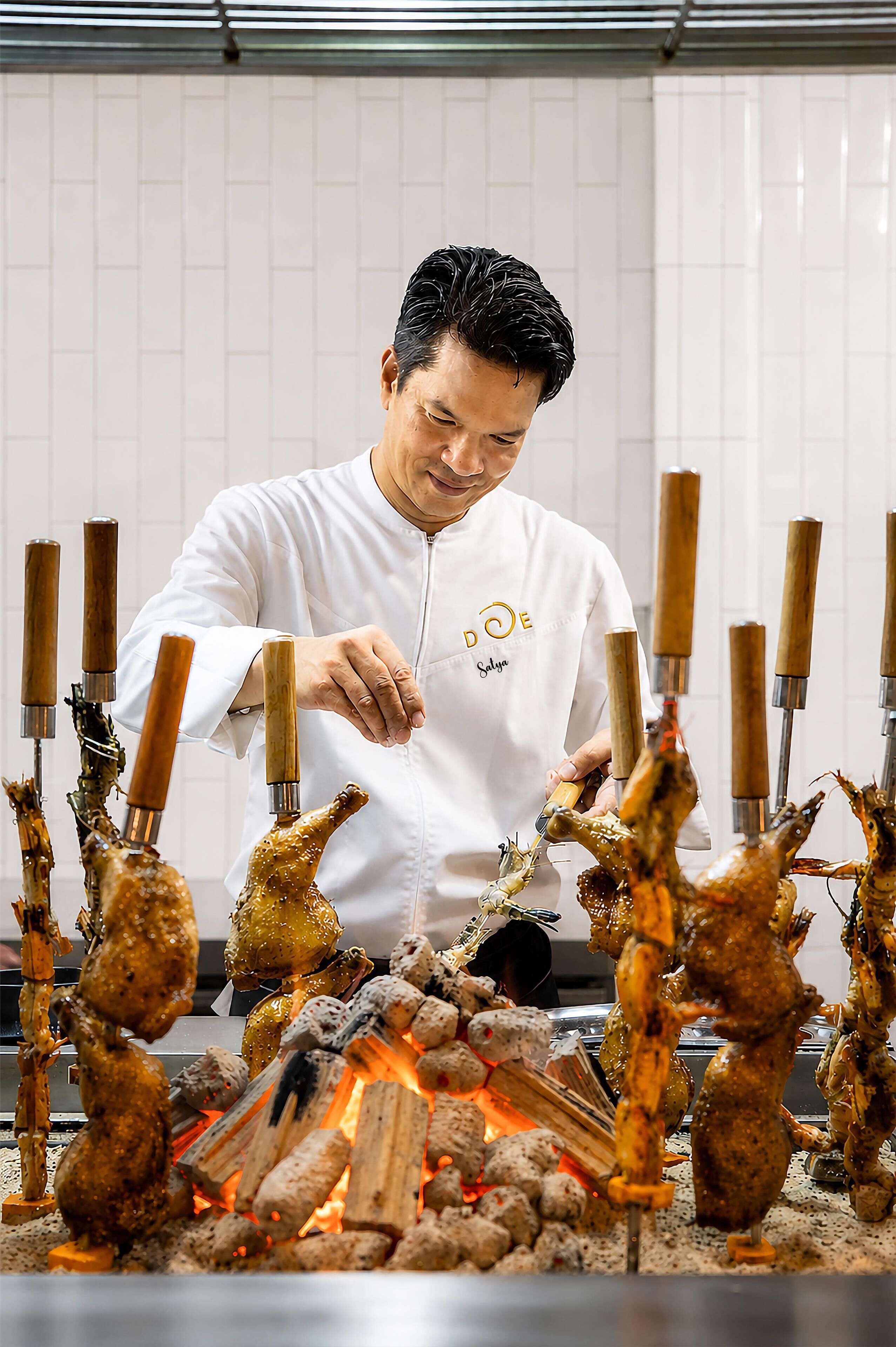A chef preparing food with skewers over an open flame.