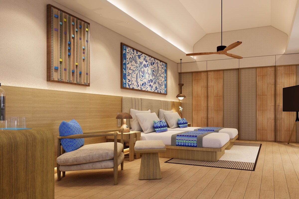 Une chambre moderne avec une tête de lit en bois, un grand lit agrémenté d’oreillers à motifs, une table de chevet, une chaise, une lampe sur pied et un ventilateur de plafond.