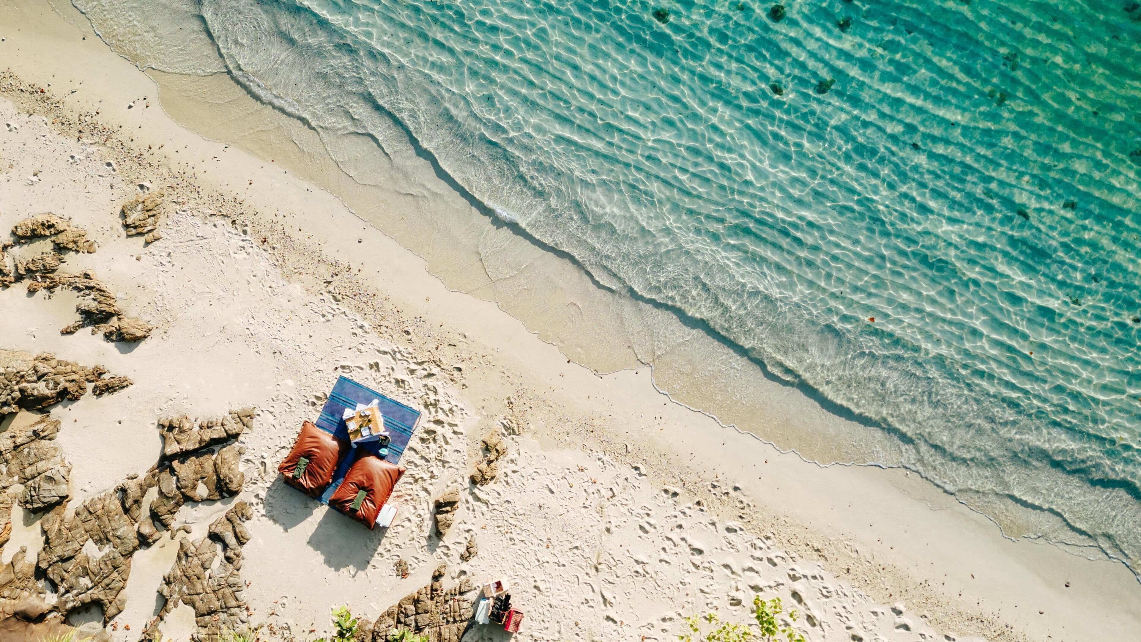 A beach with clear water, a person lying on a towel, and scattered rocks.