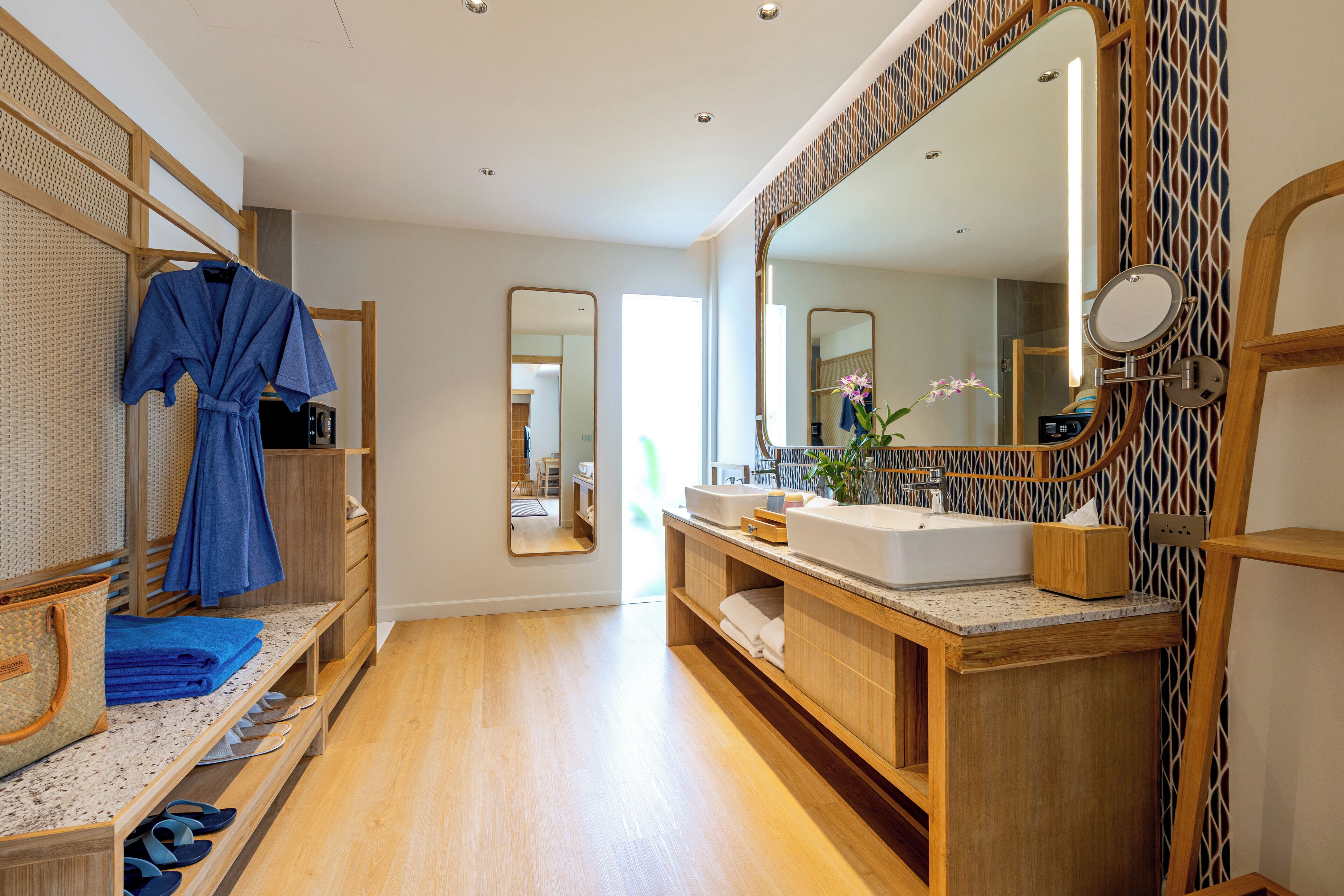 A modern bathroom with a wooden vanity, a large mirror, and a robe hanging on a rack.