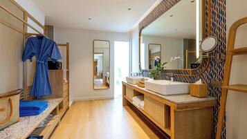 A modern bathroom with a wooden vanity, a large mirror, and a robe hanging on a rack.