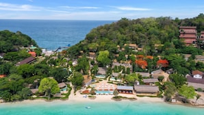 Vista aérea de un complejo turístico frente a la playa con villas, una zona de piscina y abundante vegetación.