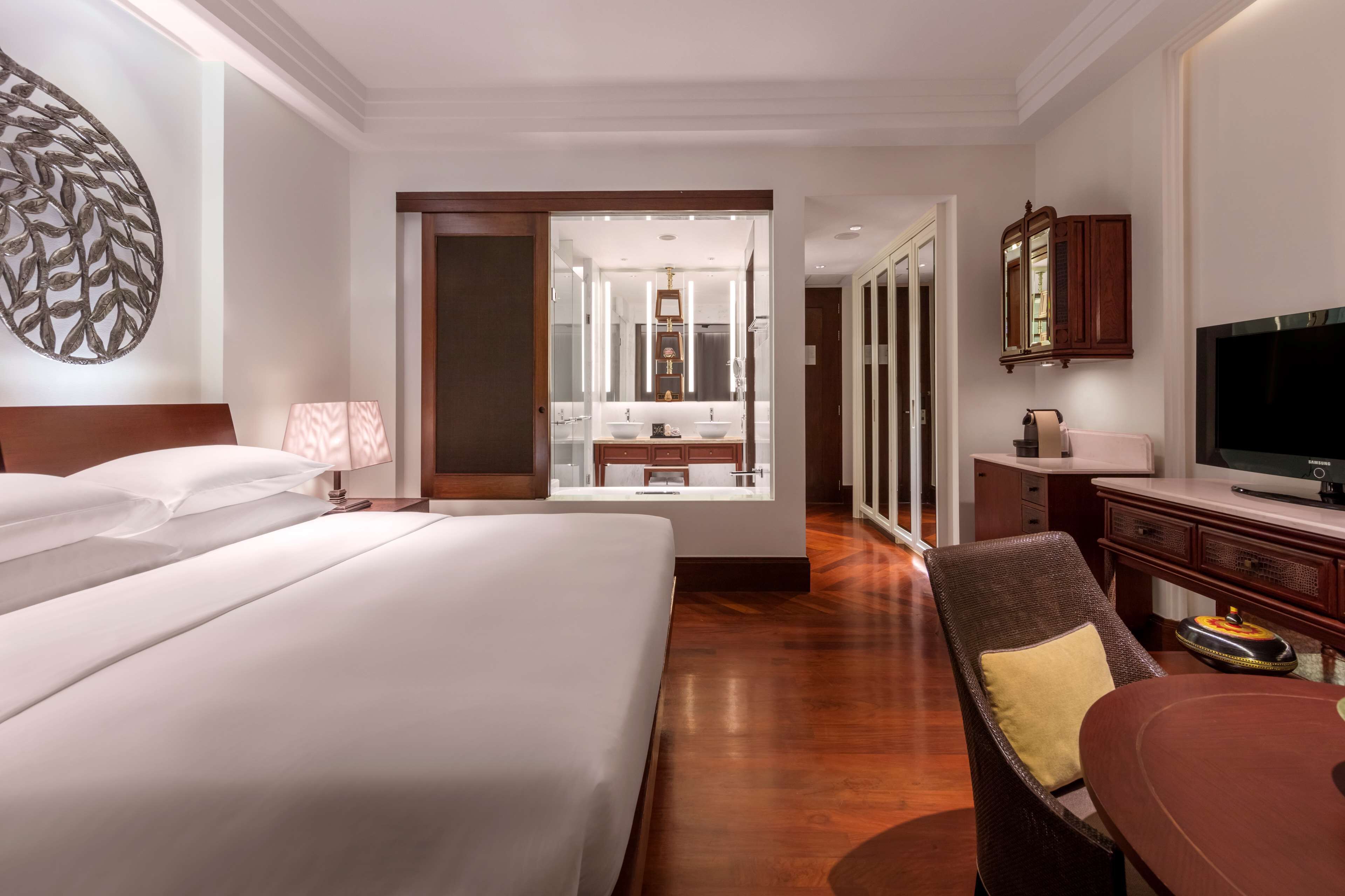 Ein Hotelzimmer mit einem großen Bett, einem Schreibtisch mit Fernseher, einem Sessel und einem durchgegangene Tür erkennbaren Badezimmer.