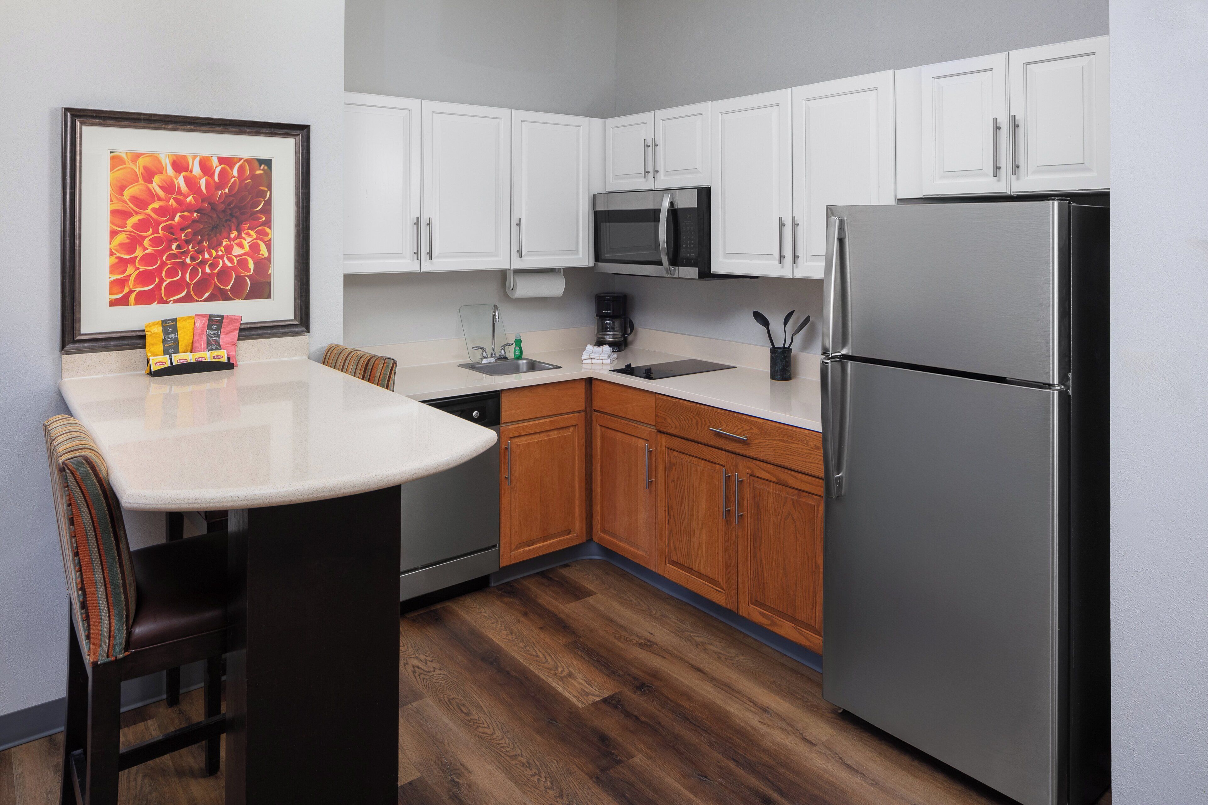 A kitchen with white cabinets, a stainless steel refrigerator, a microwave, and a coffee maker.
