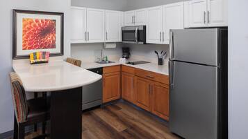 A kitchen with white cabinets, a stainless steel refrigerator, a microwave, and a coffee maker.