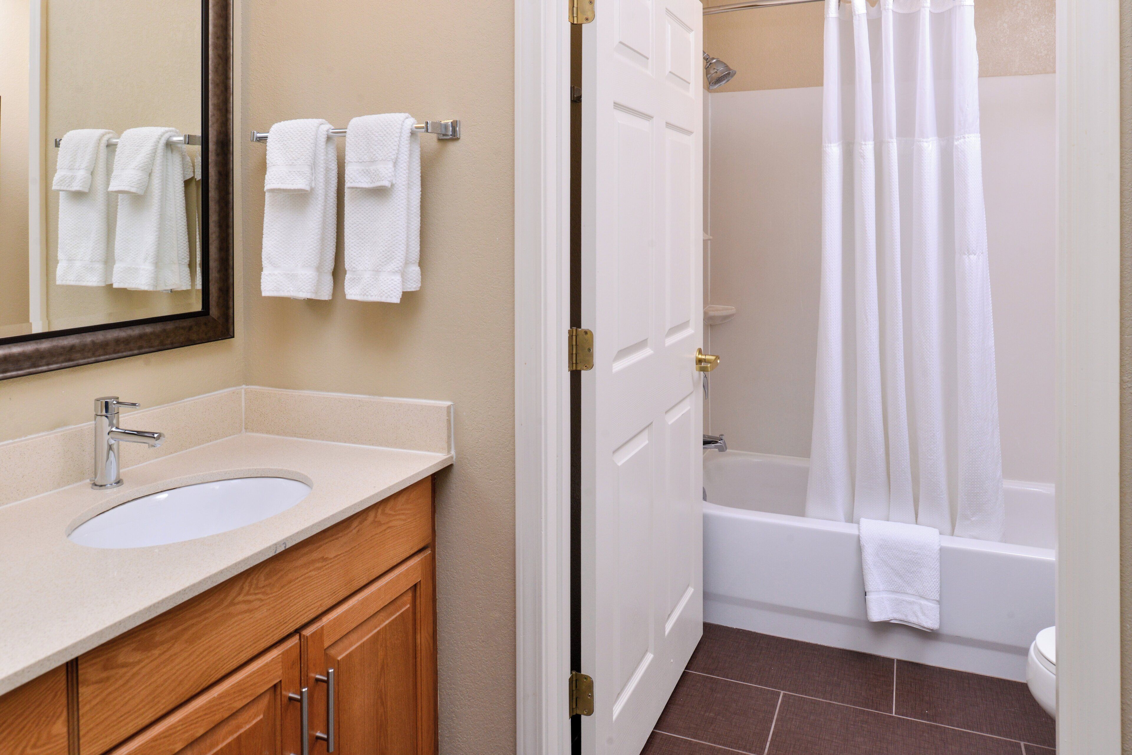 A bathroom with a sink, mirror, wooden cabinets, a shower curtain, and a bathtub.