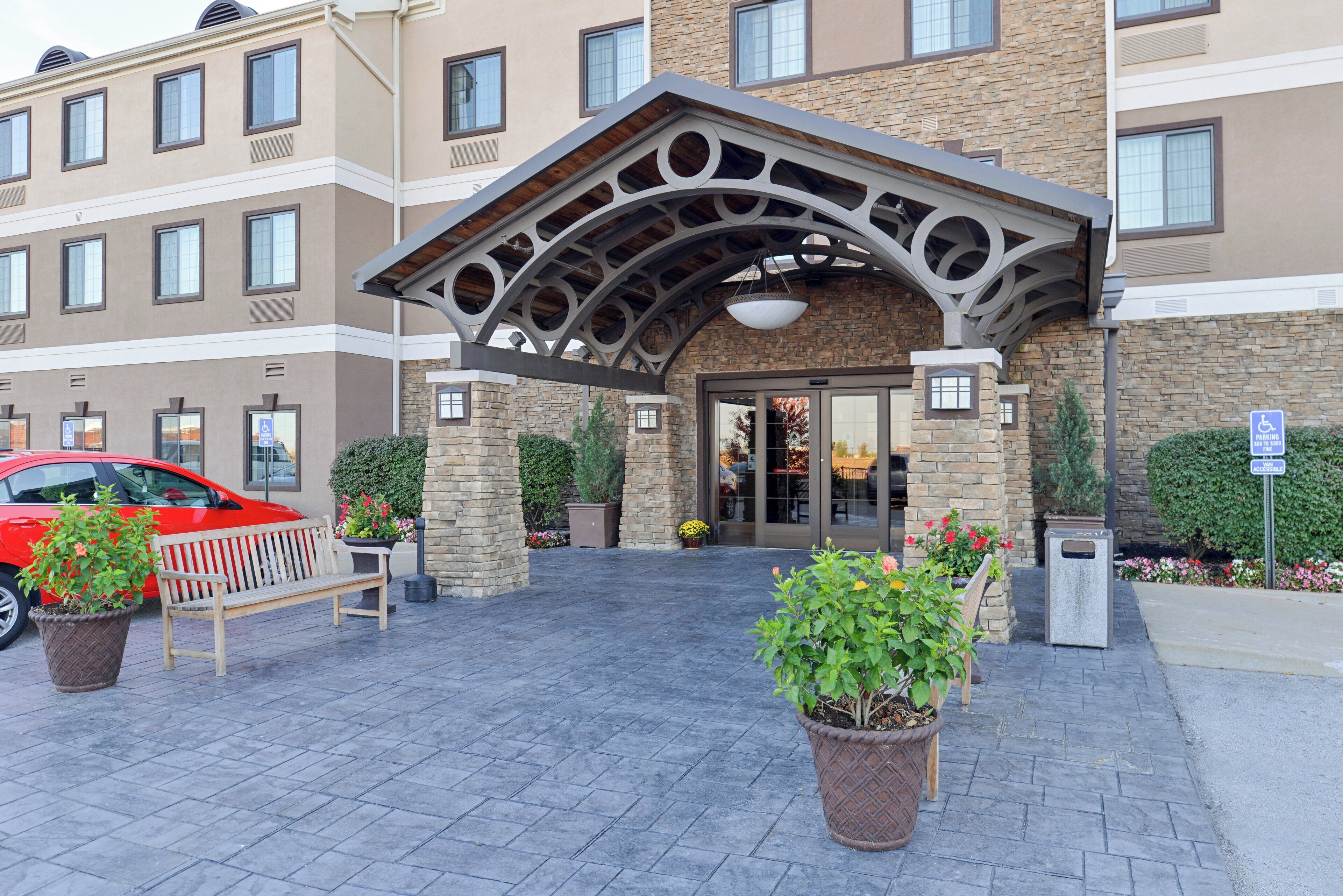 Ein Hotel mit steinverkleideter Fassade, einem überdachten Eingangsbereich und Blumentöpfen.