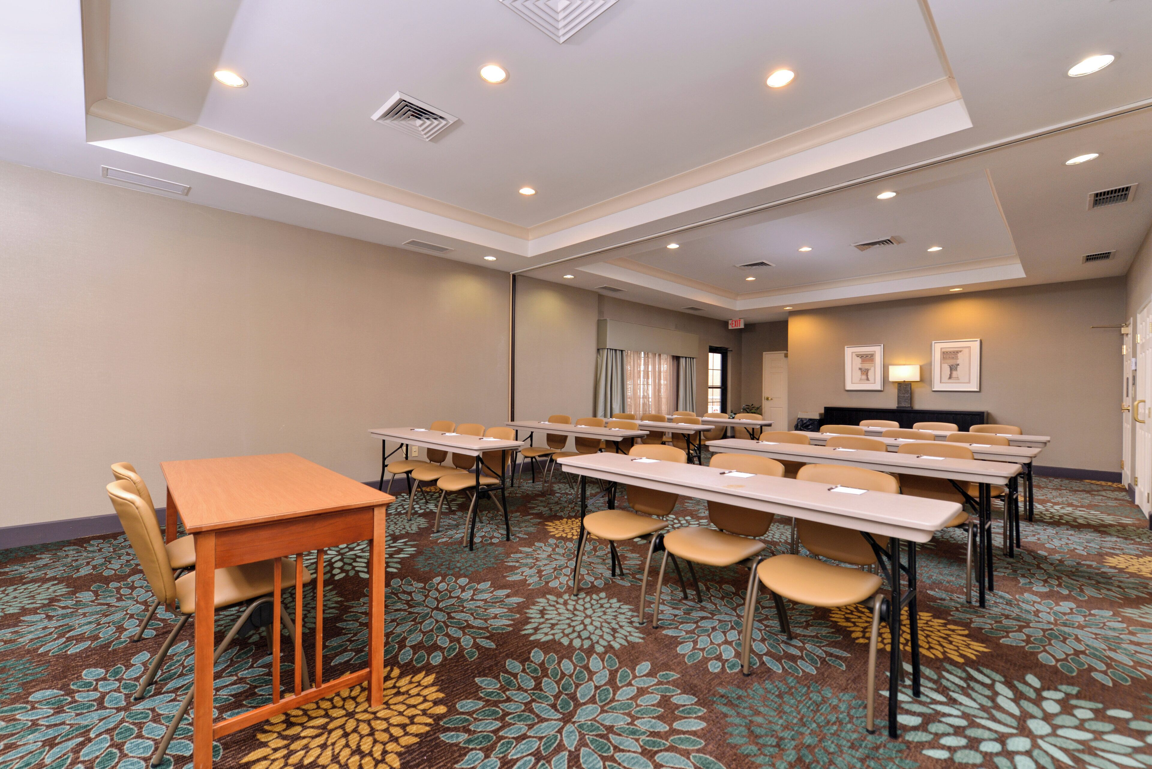 A conference room with multiple tables and chairs, carpeted floor, and ceiling lights.
