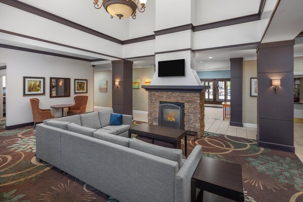 A hotel lobby with a sectional sofa, a fireplace, a flat-screen TV, and framed artwork on the walls. - Staybridge Suites O'Fallon Chesterfield by IHG (O'Fallon)