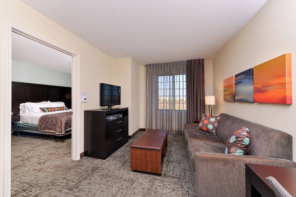 A hotel room with a bed, a TV, a sofa, a desk, and a window with curtains.
