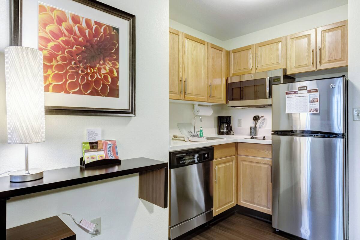 A modern kitchen with wooden cabinets, stainless steel appliances, and a framed floral artwork on the wall.