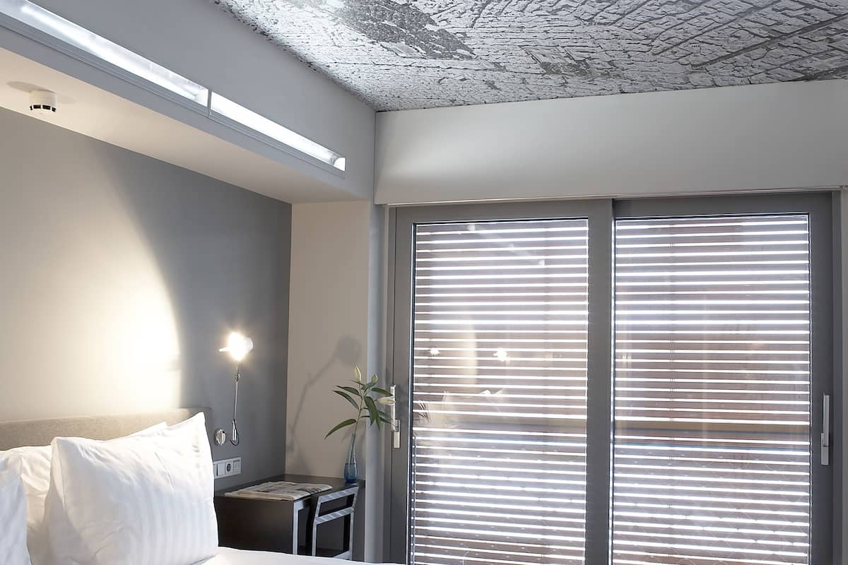 A modern hotel room with a large bed, a nightstand, a vase with flowers, and a sliding glass door to the outside.