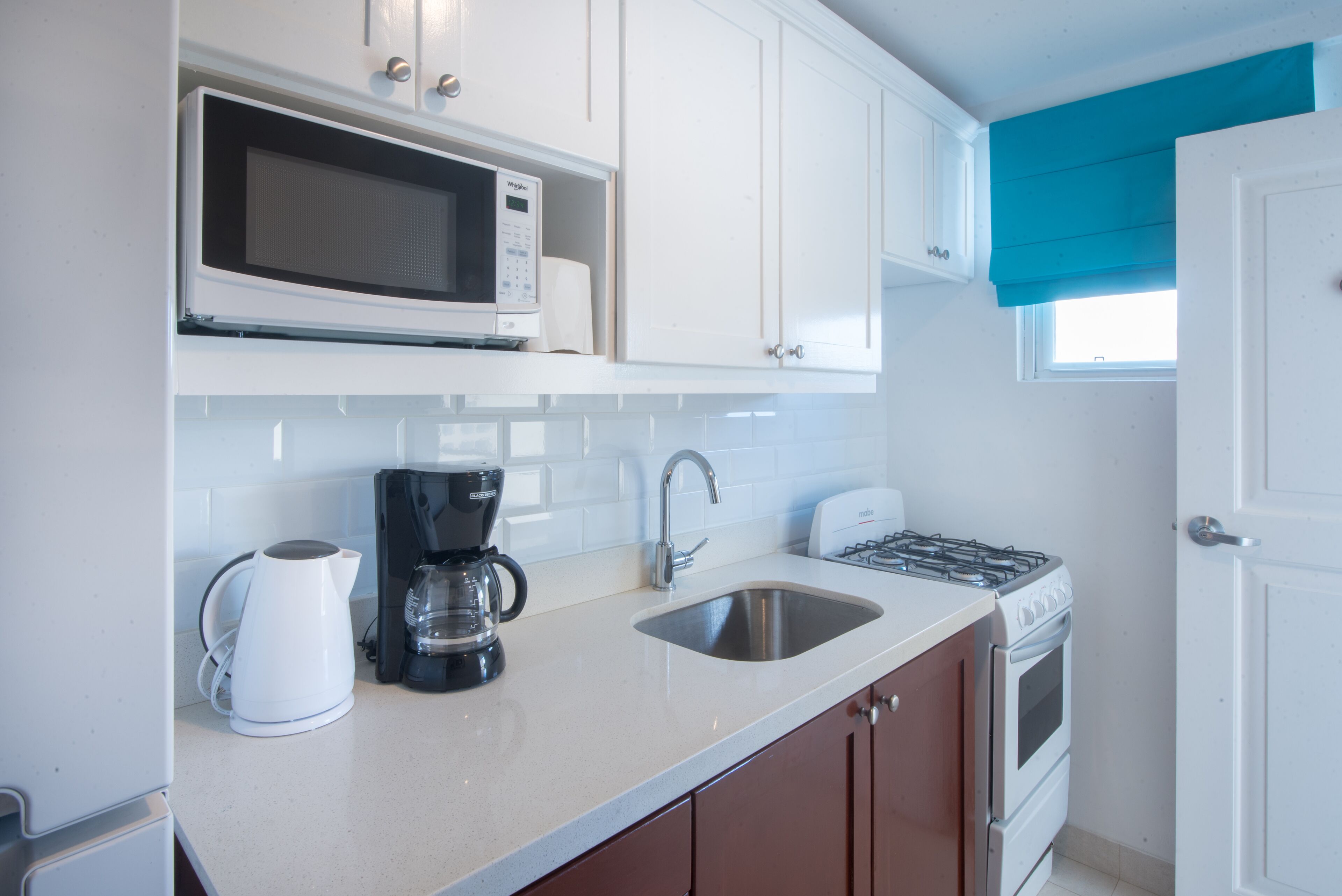 A modern kitchen with white cabinets, a microwave, a coffee maker, a sink, and a stove.