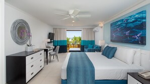 Habitación de hotel con cama, escritorio, silla, cómoda, ventilador de techo y una ventana grande con cortinas.