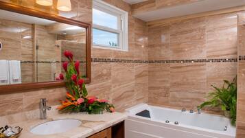 A bathroom with a marble wall, a sink, a mirror, a shower, and a potted plant.
