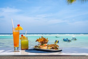 A table with a drink, a jar, a basket of fries, and a plate of food with a flag. - Yellow Bird Hotel (St. Lawrence Gap)