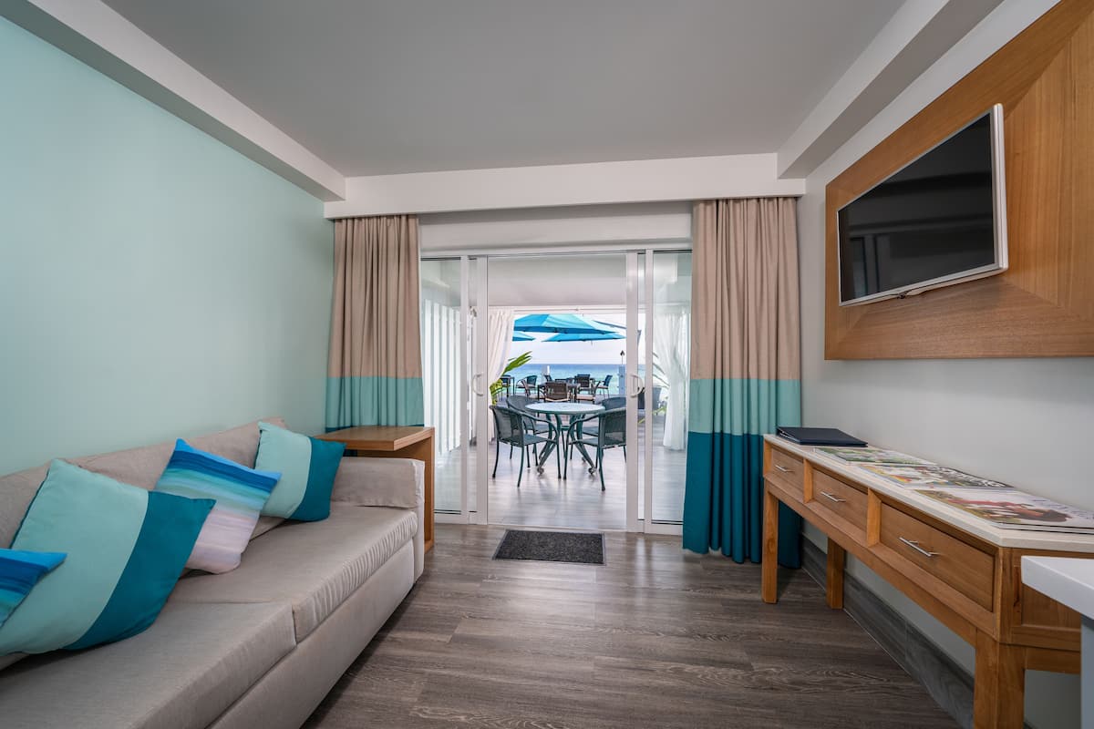 Sala de estar moderna com sofá, televisão na parede, escrivaninha de madeira e vista para a varanda através de portas de vidro.