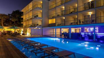 A multi-story hotel with a swimming pool, outdoor seating, and a bar area.