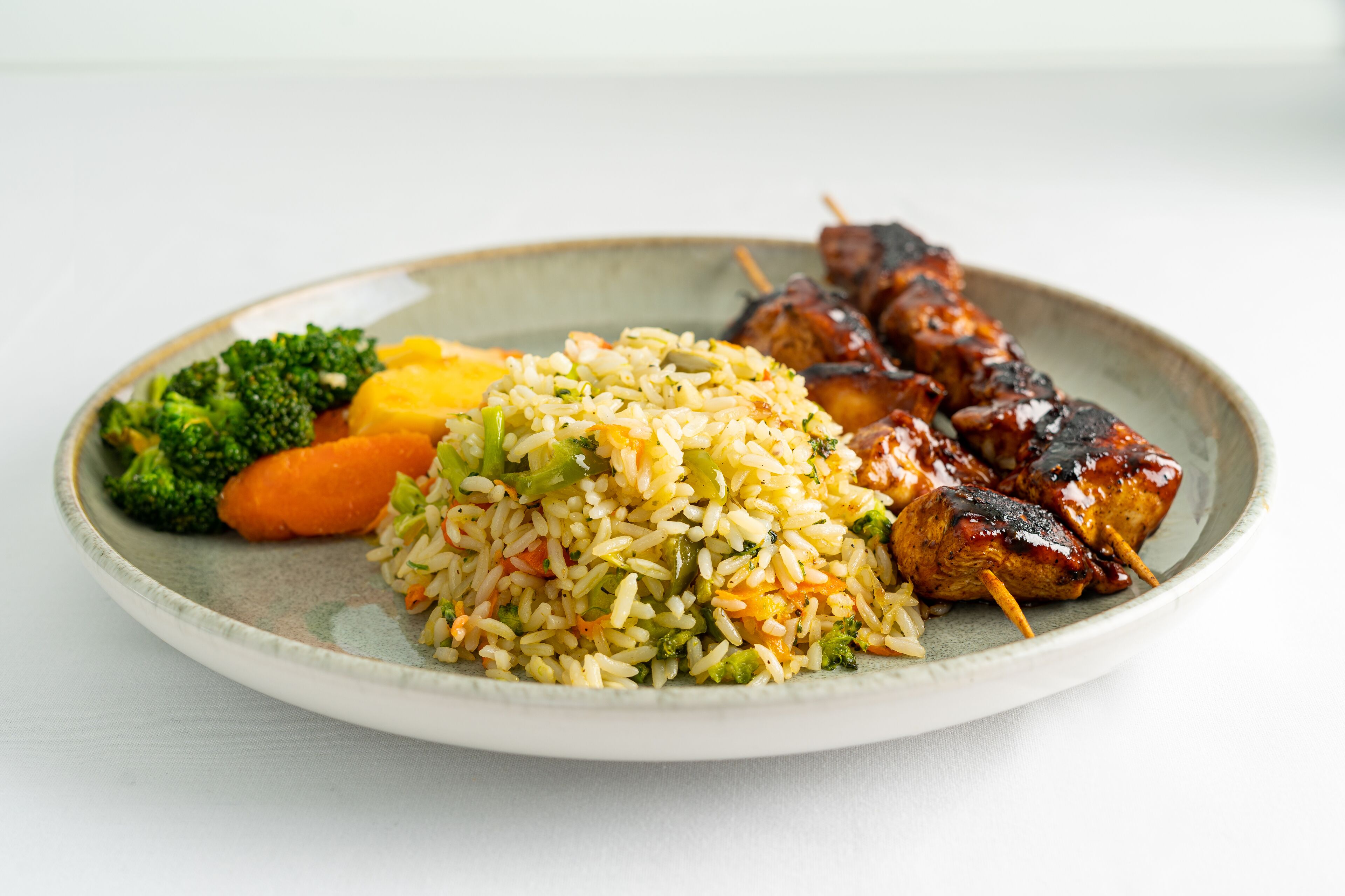 A plate with fried rice, vegetables, and grilled meat skewers.