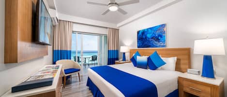Ein Hotelzimmer mit Bett, Schreibtisch, Stuhl, Fernseher, Deckenventilator und einem Fenster mit Meerblick.