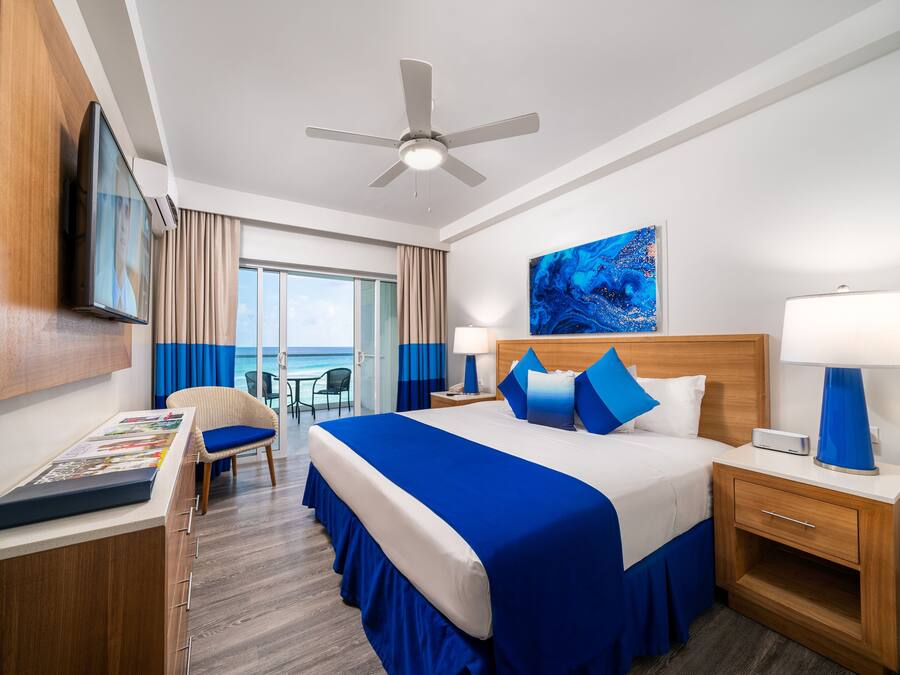 Habitació d'hotel amb llit, escriptori, cadira, televisió, ventilador de sostre i finestra amb vista a l'oceà.