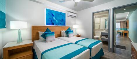 A hotel room with two beds, a ceiling fan, a large window, and a bathroom visible through an open door.