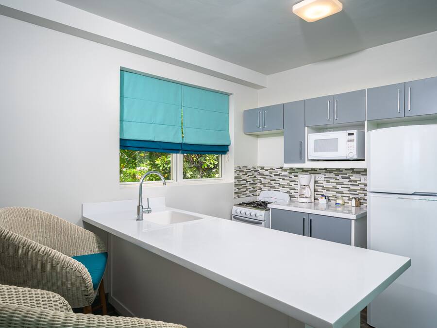 A modern kitchen with a white countertop, grey cabinets, a teal window blind, a white stove, and a white refrigerator.