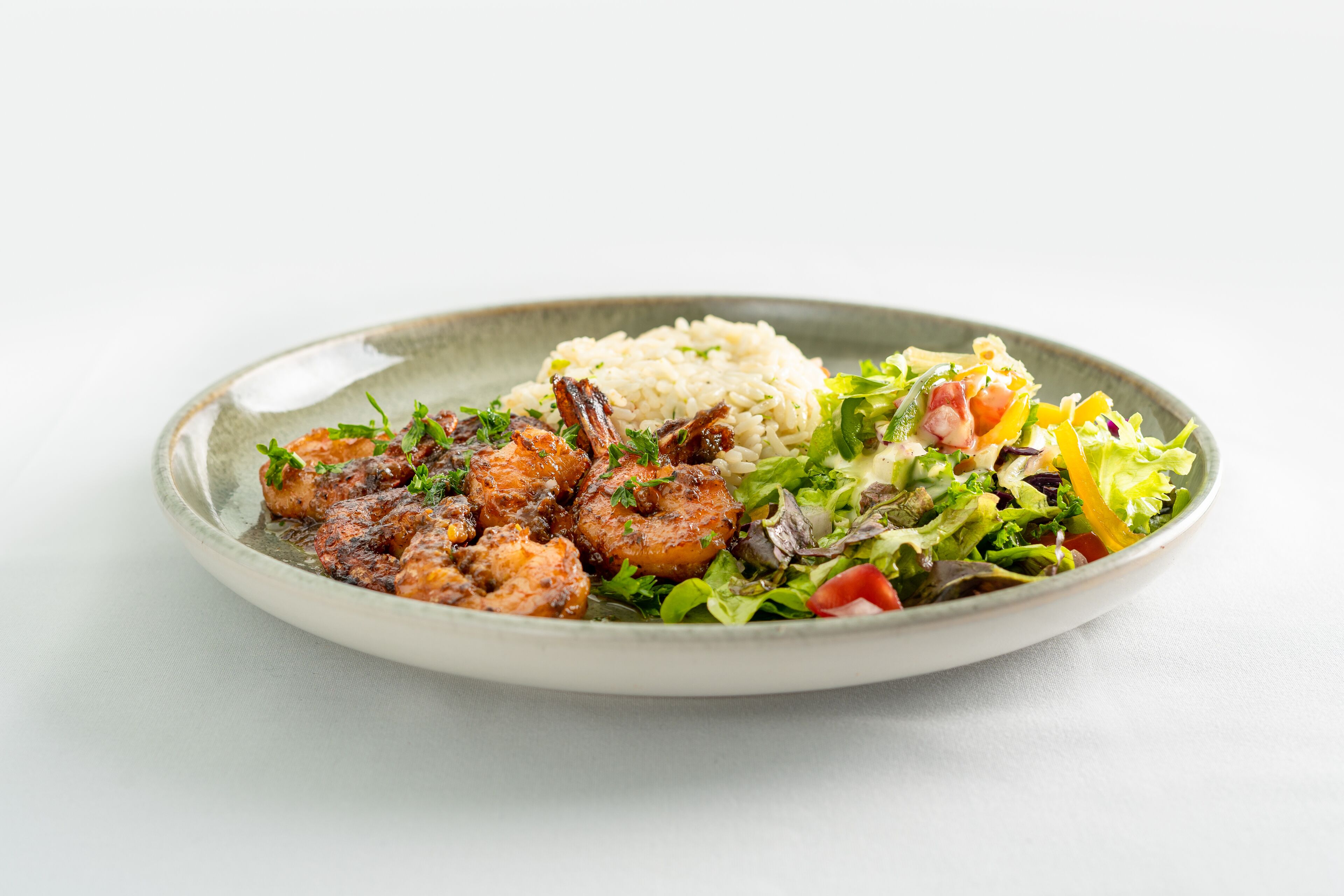 A plate with grilled shrimp, rice, and a mixed green salad.