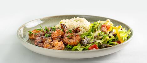 Une assiette comprenant des crevettes grillées, du riz et une salade composée.