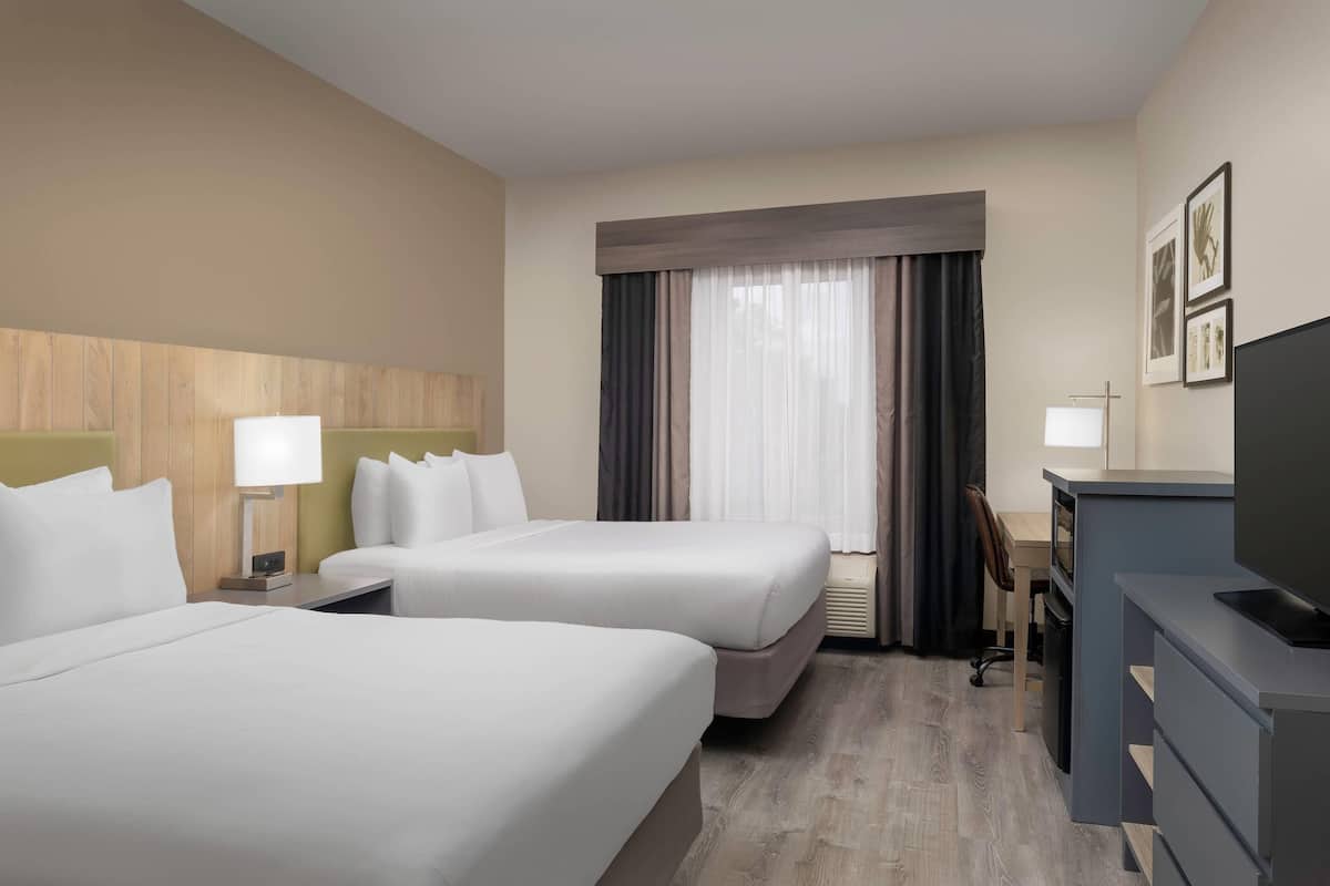 A hotel room with two beds, a desk, a television, and a window with curtains.