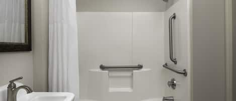Une salle de bain moderne avec un lavabo blanc, une douche équipée de barres d’appui et un miroir doté d’un cadre décoratif.