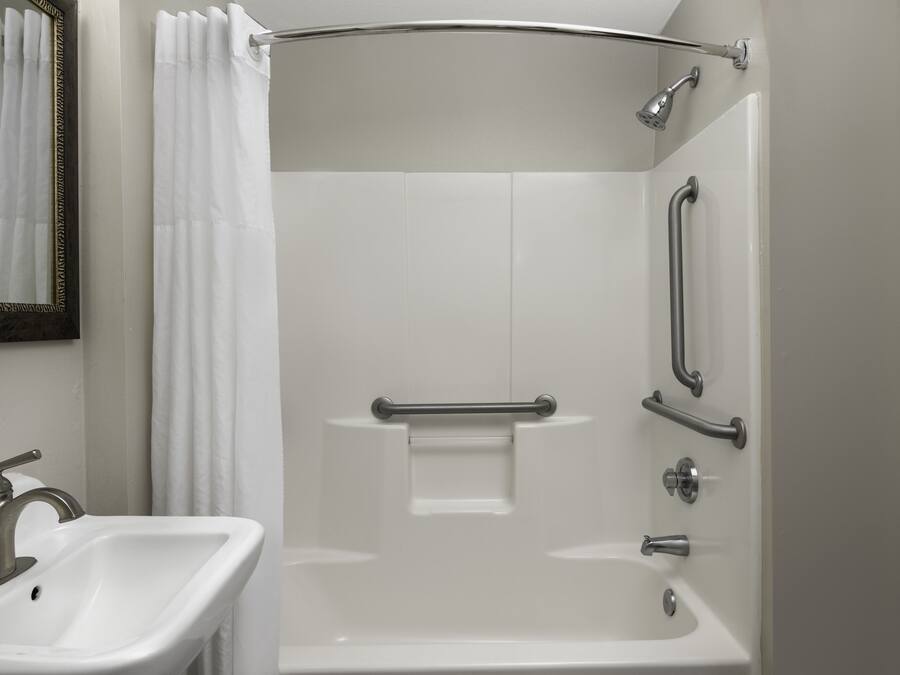 A modern bathroom with a white sink, a shower with grab bars, and a mirror with a decorative frame.