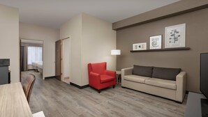 A hotel room with a wooden floor, a red armchair, a beige sofa, a TV, and framed artwork on the wall. - Country Inn & Suites by Radisson, Gainesville, FL (Gainesville)