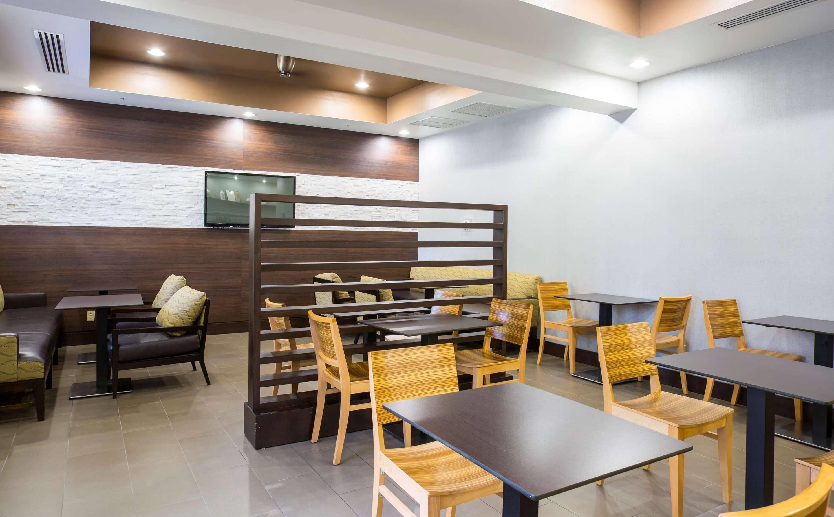 A modern restaurant with wooden furniture, a TV mounted on the wall, and a white brick accent wall.